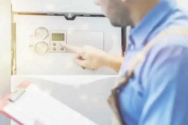 A Seatown Electric Plumbing Heating and Air technician in a blue shirt checks a wall-mounted boiler, clipboard in hand.